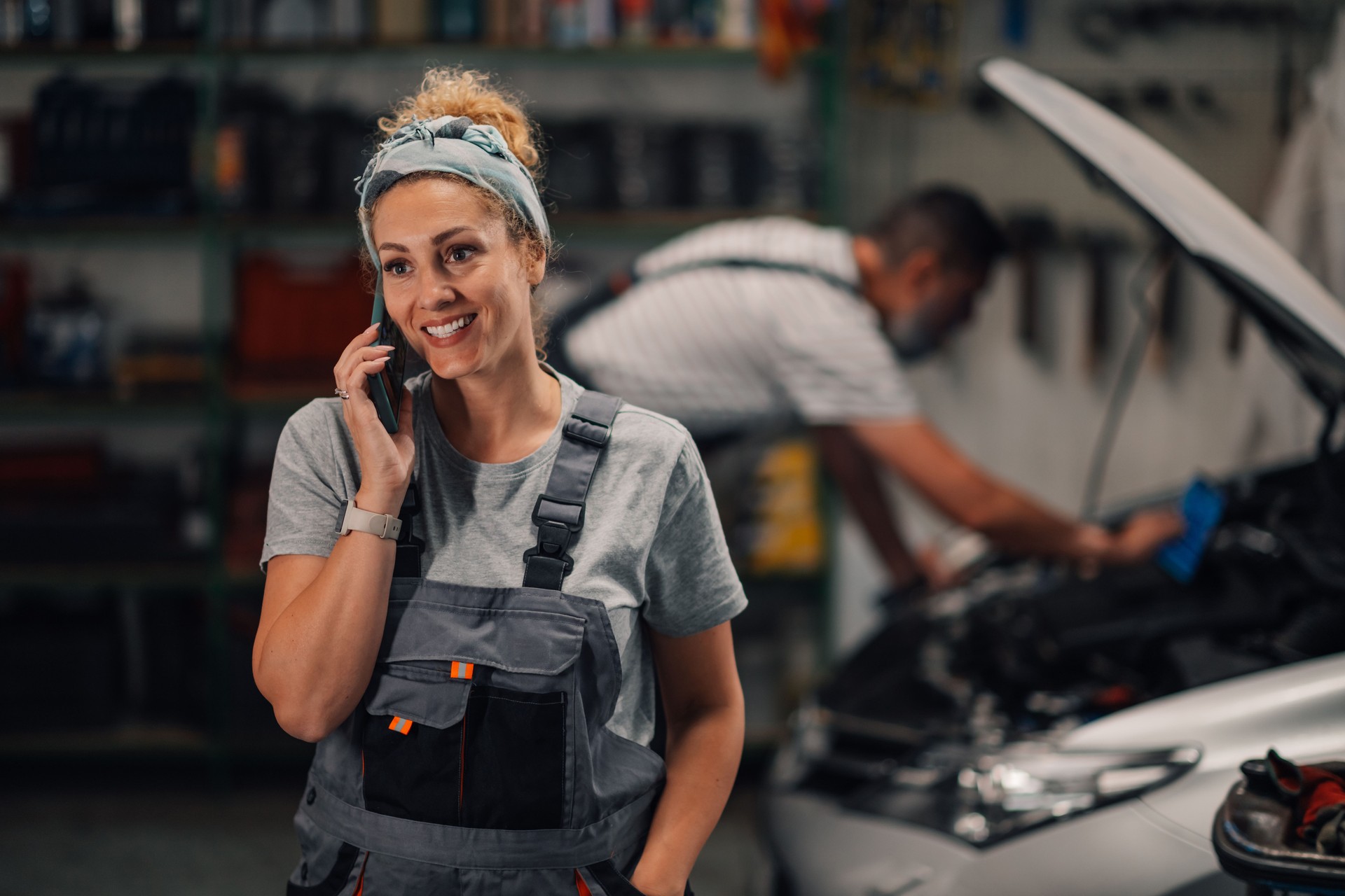 Female auto mechanic is talking on the phone with client at workshop.