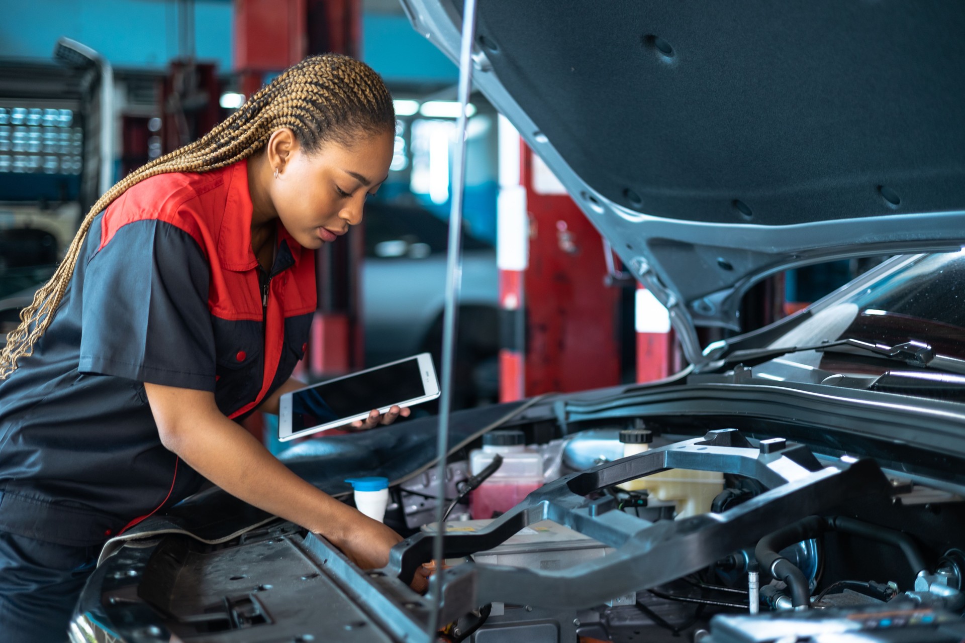 Auto service, repair, maintenance concept. Mechanic checks the car at the service station.African american woman  and asian engineer use tablet check car battery .